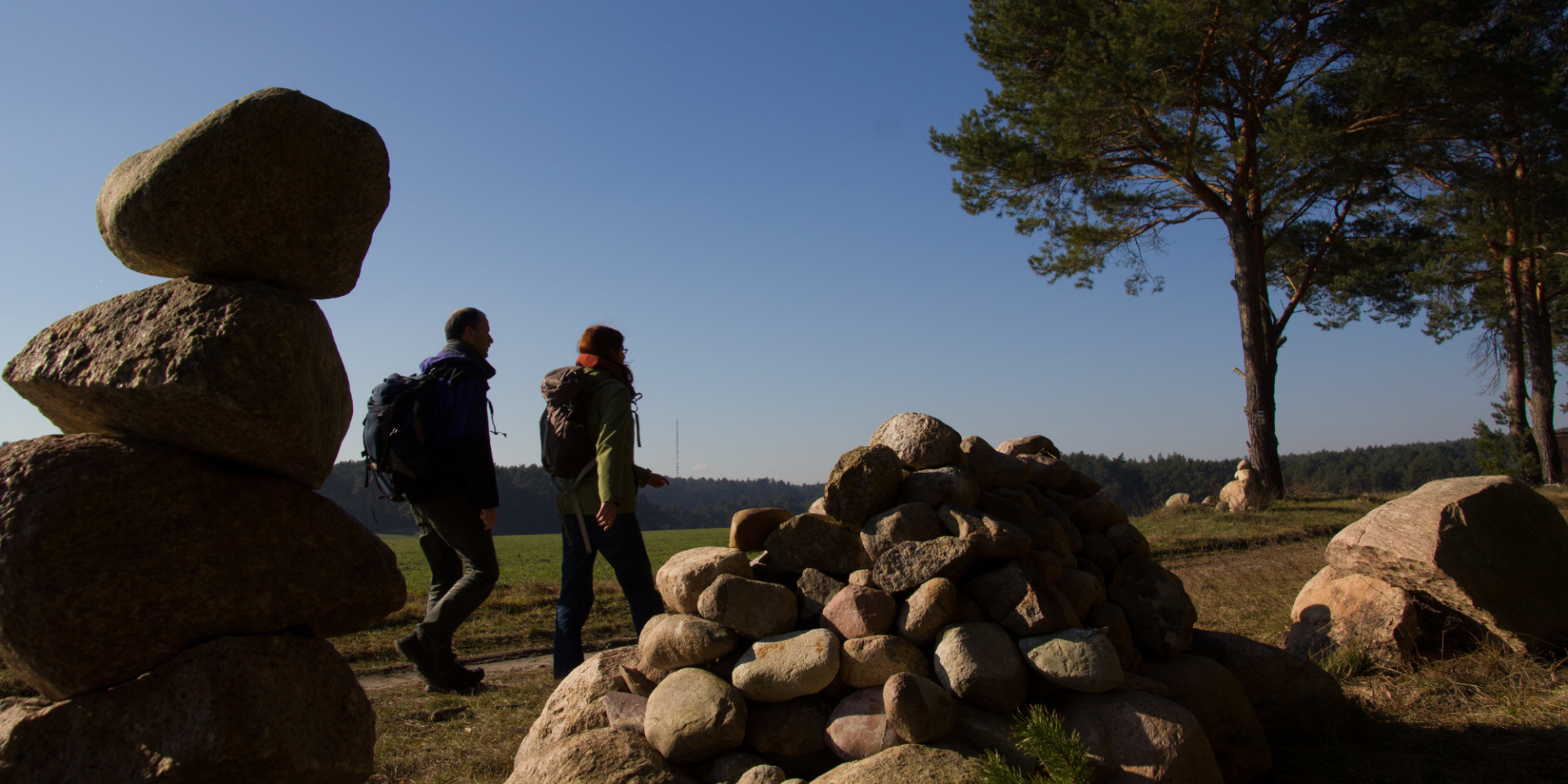 Blick durch zwei aufgeschichtete Feldsteinhaufen auf ein Wanderpaar