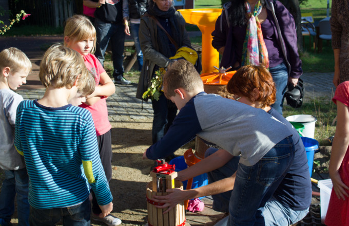 Kinder umringen eine kleine Saftpresse aus Holz