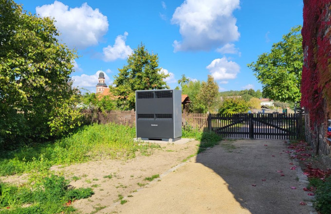 Ein grauer Kasten (die Wärmepumpe) mit Blick auf die Rabener Fachsteinkirche